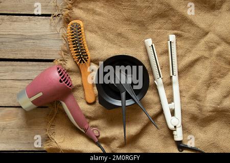 Asciugacapelli, pinze regolabili e pettini con spazzole sono appoggiati su un tavolo di legno, un set di parrucchieri è adagiato su un tavolo in un salone di bellezza, cura dei capelli Foto Stock