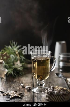Un bicchiere di tè verde con fumante e decorazione di Natale su tavolo di legno. Scuro Moody, tempo di inverno. Spazio di testo. Orientamento verticale Foto Stock