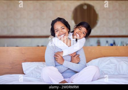 Giovane felice misto razza madre e sua figlia utilizzando un tablet digitale insieme in una camera da letto. Mamma ispanica che insegna a sua figlia come usare un Foto Stock