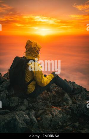 Uomo seduto sul Mountain Peak che si gode il tramonto Foto Stock