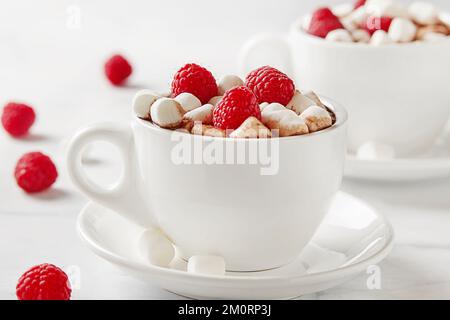Due tazze di cioccolata calda con marshmallows in miniatura, lamponi freschi e cioccolato Foto Stock