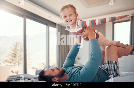 Adorabile bambina sollevata in aria da suo padre. Allegro papà sdraiato a letto e giocare con la figlia a casa. Legame di padre e figlia Foto Stock