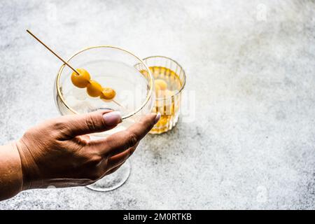 Primo piano di una donna che si avvicina per un cocktail di vodka e un tumbler riempito di ciliegie giallo glace Foto Stock