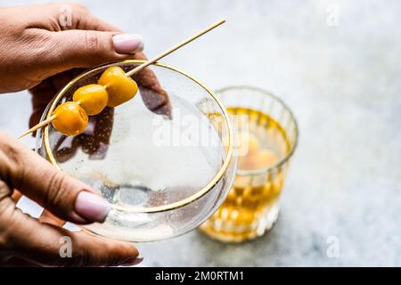 Primo piano di una donna che si avvicina per un cocktail di vodka e un tumbler riempito di ciliegie giallo glace Foto Stock