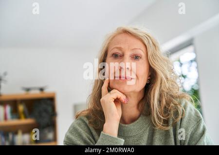 Donna anziana premurosa con la mano sul mento seduta nella sala da pranzo Foto Stock