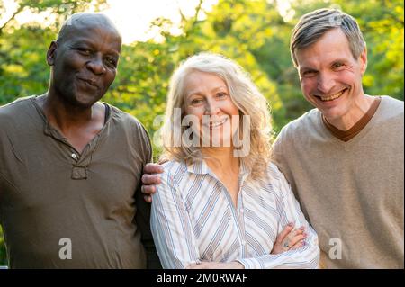 Signora anziana in posa con i suoi due amici maschi mentre si stende nel suo cortile al tramonto Foto Stock