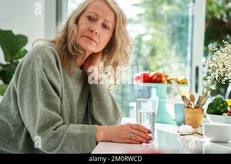 Donna anziana premurosa con mano dietro il collo seduta nella sala da pranzo Foto Stock