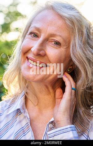 Donna anziana allegra che guarda e sorride davanti alla telecamera Foto Stock