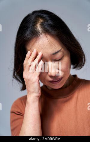 Mature Asian woman having a headache Foto Stock