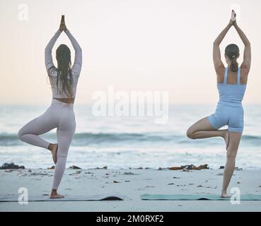 Yoga, fitness amici e allenamento in spiaggia con albero posa all'aperto nella natura per zen, pace ed equilibrio con la consapevolezza dalla meditazione. Donne insieme Foto Stock