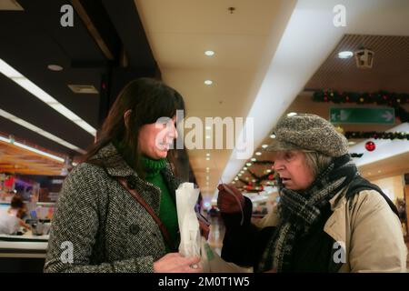 donna anziana europea e giovane adulta ispanica che controlla il conto drogherie shopping list al supermercato uscita negozio Foto Stock