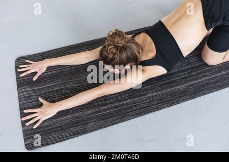 Giovane donna che pratica yoga, facendo una variazione di ashtanga namaskarasana esercizio, allenandosi in nero sportswear in una stanza su un tappetino Foto Stock