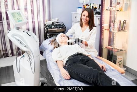 Kiev, Ucraina - 26 dicembre 2020: Donna cosmetologa che usa Ultraformer dispositivo e sorridente mentre esegue la procedura di sollevamento SMAS. Foto Stock