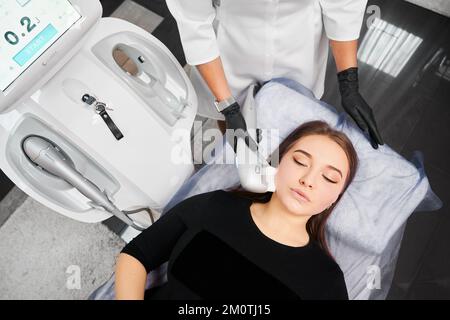 Kiev, Ucraina - 26 dicembre 2020: Vista dall'alto della giovane donna alla reception estetista in clinica. Concetto di procedura di processo per migliorare la pelle del viso da Ultraformer Foto Stock