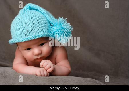 Rivne, Ucraina 25 aprile 2022: Un bambino neonato con un cappuccio blu giace sullo stomaco, ritratto da vicino. Foto Stock