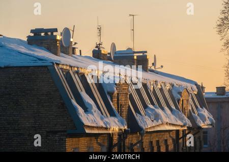 TV e antenne via cavo sul tetto di una casa di appartamenti coperta di neve al tramonto. Foto Stock