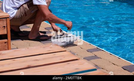 Un uomo controllerà la qualità dell'acqua. Controllare la qualità dell'acqua di piscina con un kit di test chimico in estate. PH, cloro e bromo Foto Stock
