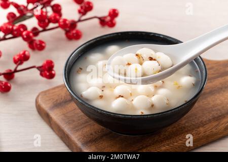 Piccolo tangyuan bianco (tang yuan, palle di gnocchi di riso glutinoso) con miele di osmanthus dolce e zuppa di sciroppo in una ciotola su fondo di tavolo di legno. Foto Stock