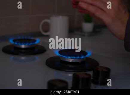 Una donna riscalda le mani vicino al gas in cucina. Bassa temperatura in camera, aumento dei prezzi per il riscaldamento, freddo nel concetto di appartamento. cri. Energia Foto Stock