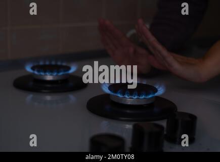 Una donna riscalda le mani alla stufa a gas a casa. Mancanza di elettricità e calore nelle case dei cittadini. Crisi energetica, conseguenze delle ostilità, Foto Stock