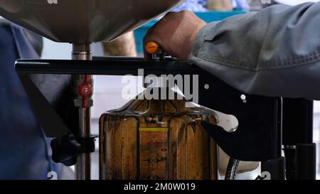 Sostituire l'olio motore. Le mani maschili di un meccanico scaricano l'olio vecchio dalla vettura in un apposito contenitore. Olio sporco vecchio scaricato da sotto A. Foto Stock