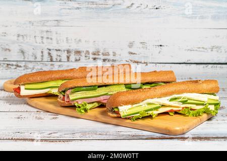 Varietà di deliziosi panini baguette su tagliere. Salame, carne affumicata, olive, lattuga, sandwich di pomodoro e cetriolo Foto Stock
