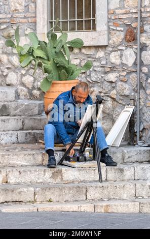 Artista con il cavalletto e le pitture, seduto su gradini a Taormina. Sicilia, Italia Foto Stock