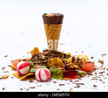 Cialda di gelato ripiena di salsa di cioccolato o cono di waffle circondato da cialde di cioccolato caramelle bianche rosse e dolci di gelatina su sfondo bianco Foto Stock