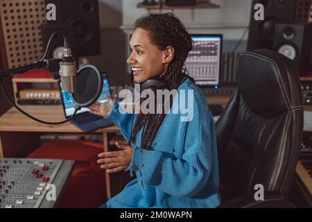 Il presentatore radiofonico piacevole multietnico registra i podcast usando le cuffie e parlando nel microfono in uno studio di registrazione Foto Stock