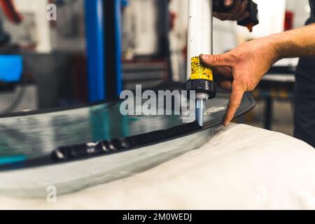 Veicoli e concetto di macchina. Montaggio del finestrino dell'auto. Primo piano ritratto della pistola per colla caucasica e applicazione di colla nera sulla superficie del lunotto. Foto di alta qualità Foto Stock