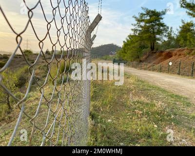 recinzione di ferro e filo spinato parallelo alla strada sterrata. tramonto in campagna. fuoco selettivo sulla parete della recinzione. Foto Stock