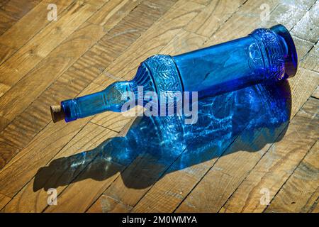 Una bottiglia di vetro blu giacente sul terreno trafitto dai raggi del sole Foto Stock