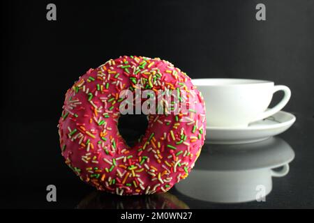 Doughnut con glassa rosa berliner si trova accanto a una tazza di caffè tè deliziosa prima colazione snack giorno senza dieta su sfondo nero copyspace Foto Stock