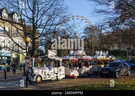 Gli amanti dello shopping natalizio sul Candy cane Express Road Train viaggiano lungo una strada con la ruota panoramica sullo sfondo, ad Harrogate, Yorkshire, Inghilterra, Regno Unito. Foto Stock