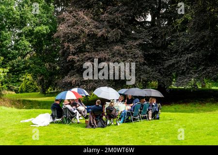 Un gruppo di persone che hanno Un picnic in the Rain, Hever Castle, Kent, Regno Unito. Foto Stock