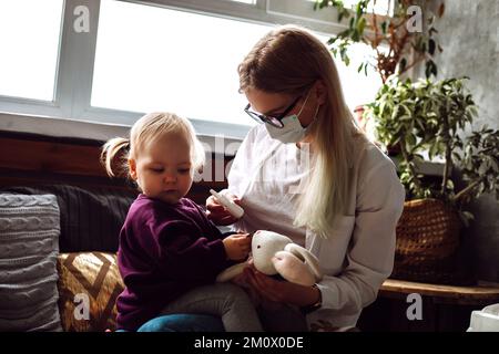 Ritratto di bambina bambino seduto sul medico bambino indossare maschera medica che si rifiuta di ottenere la medicina nasale a casa. Foto Stock