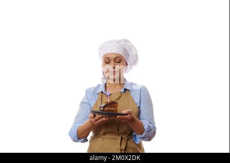 Compleanno ragazza, donna chef pasticciere tiene un piatto con torta al cioccolato, fa desiderio amato prima di soffiare fuori candela Foto Stock