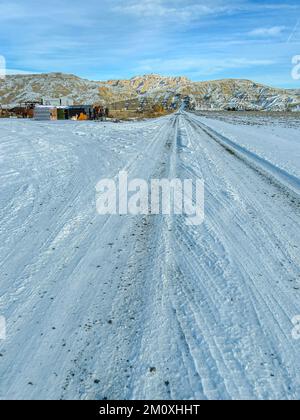 La vecchia strada di campagna nel Wyoming innevata conduce alle montagne diritto avanti. Immagine con visualizzazione verticale o ampia disponibile. La strada ha linee e tracciati di punta. Foto Stock