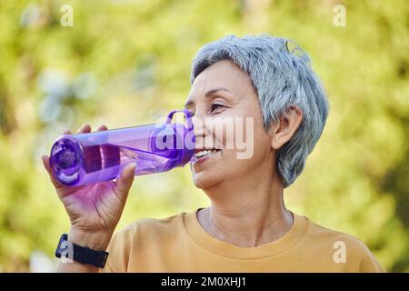 Primo piano immagine attraente donna matura tiene in plastica bottiglia riutilizzabile fare sorseggiare bere acqua minerale fermo durante il lavoro mattutino fuori o passeggiata in estate Foto Stock