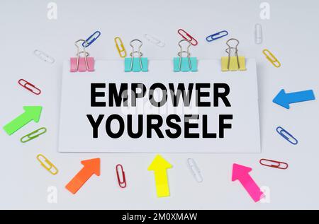 Concetto di business e finanza. Sul tavolo ci sono graffette e frecce direzionali, un segno che dice - EMPOWER TE STESSO Foto Stock