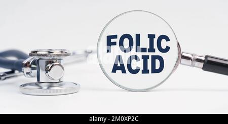 Medicina e concetto di salute. Sulla tavola è presente uno stetoscopio, una lente d'ingrandimento con l'iscrizione acido FOLICO Foto Stock