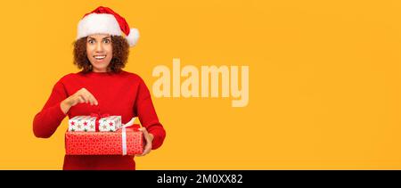 Piacevolmente eccitato felice donna tiene in mano il regalo di natale. Donna afroamericana in cappello di babbo natale Foto Stock