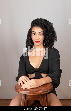 Ritratto di una giovane donna seduta, guardando seriamente la fotocamera. Su sfondo bianco in studio Foto Stock