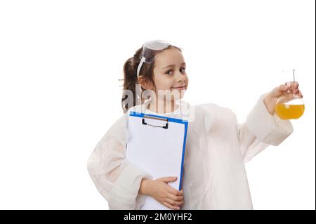 Adorabile bambina, ispirata giovane chimico-scienziato che tiene una borraccia con sostanza chimica e appunti, sul bianco Foto Stock