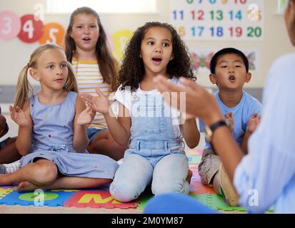 Questa canzone ci insegna su tutte le nostre parti del corpo. un gruppo di bambini che cantano in classe. Foto Stock