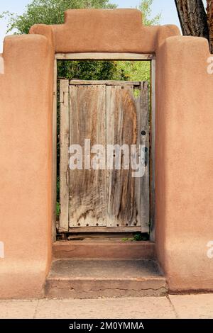 Cancello di legno intemperiato al giardino in adobe muro a Santa Fe, New Mexico Foto Stock