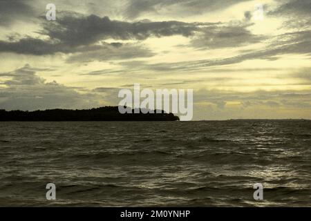 Una parte della penisola di Ujung Kulon, una parte del Parco Nazionale di Ujung Kulon, è vista da una barca che naviga intorno al tramonto in una giornata nuvolosa sullo stretto di Sunda, situata amministrativamente a Pandeglang, Banten, Indonesia. Foto Stock