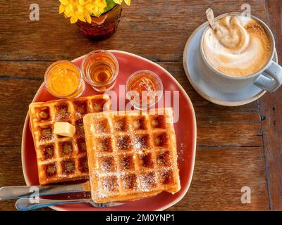 Vista dall'alto di una deliziosa colazione dolce a base di waffle belgi e caffè servita su un rustico tavolo in legno. Foto Stock