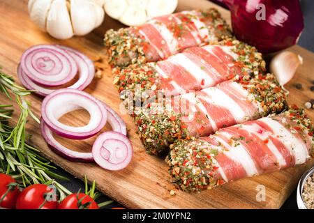 Balcanici cevapcici o romeno mitigei. Cibo tradizionale balcanico. Involtini di carne cruda macinata avvolti con pancetta con condimenti e verdure intorno al bosco Foto Stock