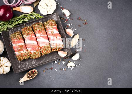 Tradizionale cibo balcanico cevapcici o rumeno mitigei pronti per grigliare o barbecue. Involtini di carne macinata cruda avvolti con pancetta e condimenti su plat nero Foto Stock